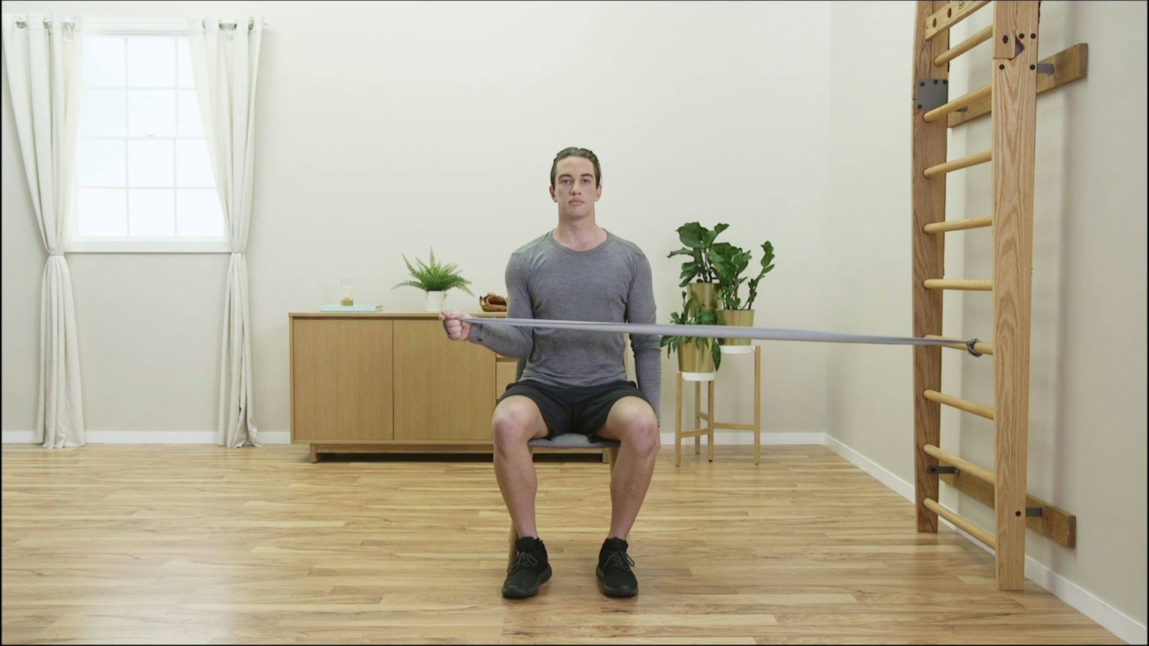 Image of a client performing shoulder external rotation in sitting with an exercise band. Screenshot from TeleHab Exercise Prescription App.